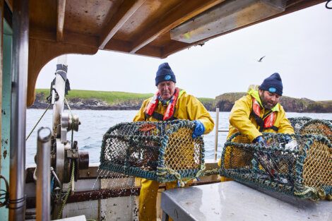 Two fishermen hauling nets on a boat.