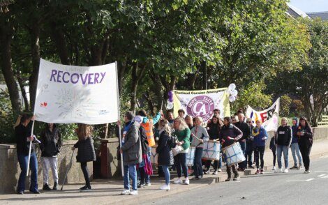 Group of individuals participating in a march with banners promoting recovery from addiction.