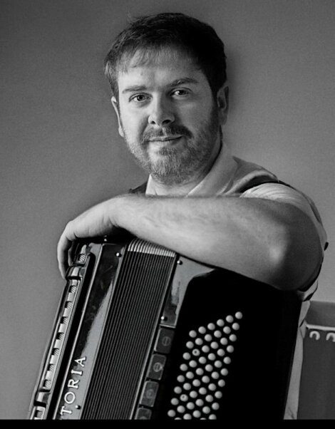 Man holding an accordion and looking at the camera with a subtle smile, in a black and white photograph.