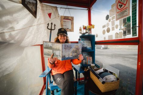 Woman in a ticket booth holding up a 'tall ship' brochure with a smile.