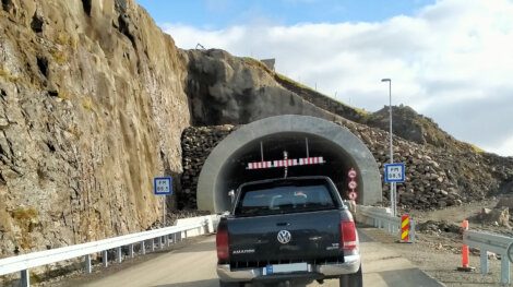 Vehicles waiting at the entrance of a single-lane tunnel with height restriction sign.