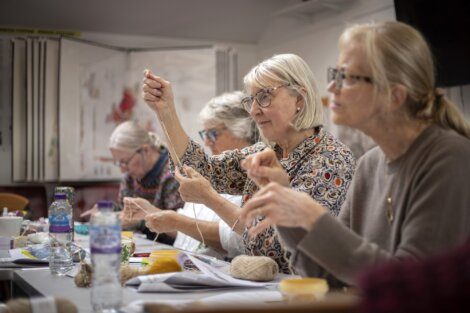 A group of women engaged in a knitting class, focusing intently on their craft.