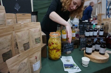 A woman is standing next to a table full of herbs and spices.