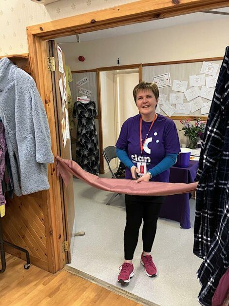 A woman cutting a ribbon in a room full of clothes.