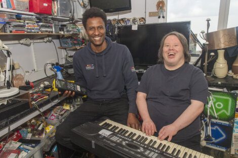 Two men sitting in a room with a keyboard.