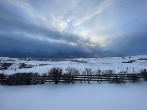 A snow covered field with a fence and clouds in the sky.