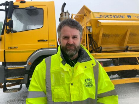 A man standing in front of a snow plow truck.