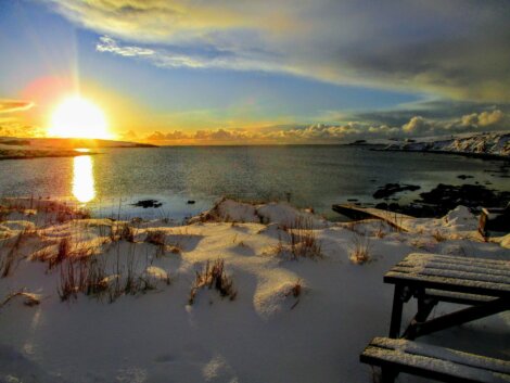 The sun is setting over a snow covered body of water.