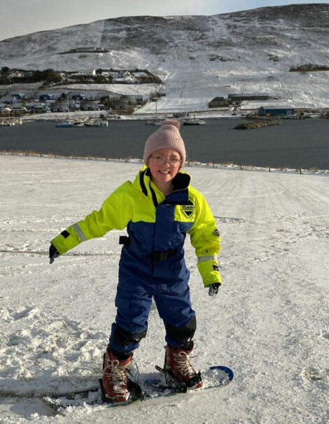 A child wearing a yellow jacket and blue pants is on skis.