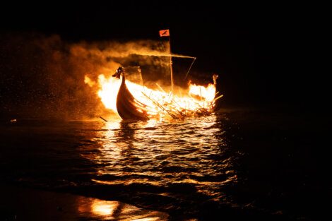 A boat engulfed in flames at night on a body of water.