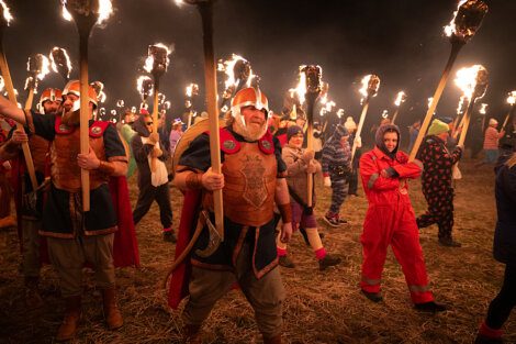 People dressed in various costumes carrying torches at a nighttime outdoor event.