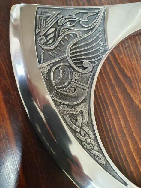 Close-up of an ornate metal axe blade with engraved patterns on a wooden surface.