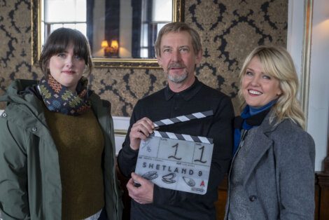 Three individuals on a film set, one holding a clapperboard with the title 