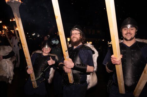 Participants dressed in viking-inspired costumes carrying torches during a nighttime event.