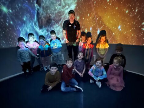 A group of children posing for a photo in front of a planetarium.