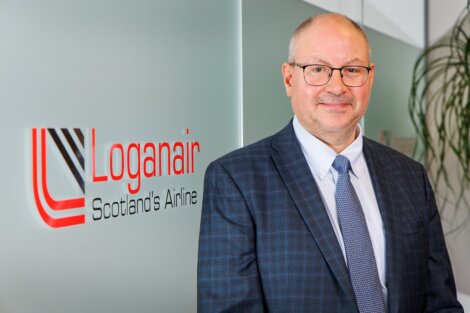 Professional in a suit posing in front of a loganair sign.