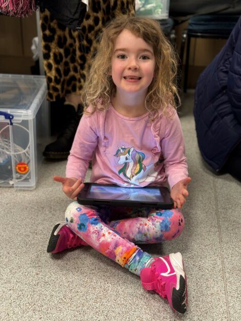 A young girl sitting on the floor with a tablet.