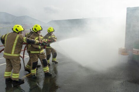 Firefighters in protective gear using a hose to spray water during a training exercise or emergency response.
